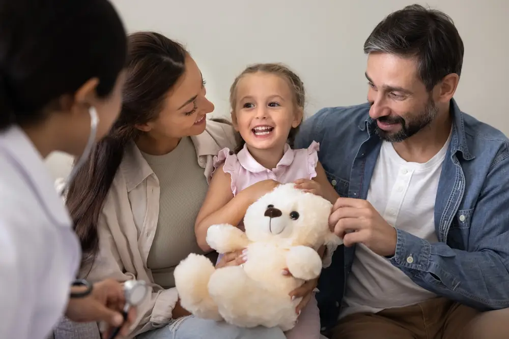 Family with a young child holding a teddy bear during a consultation